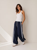 Model wearing BROCK Golden days wide-leg navy trousers with white side stripes, elastic waist, and drawstring cuffs.