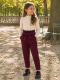Girl wearing BROCK GRASSTAR burgundy high-waisted trousers with a tie-waist and cream ribbed long-sleeve top