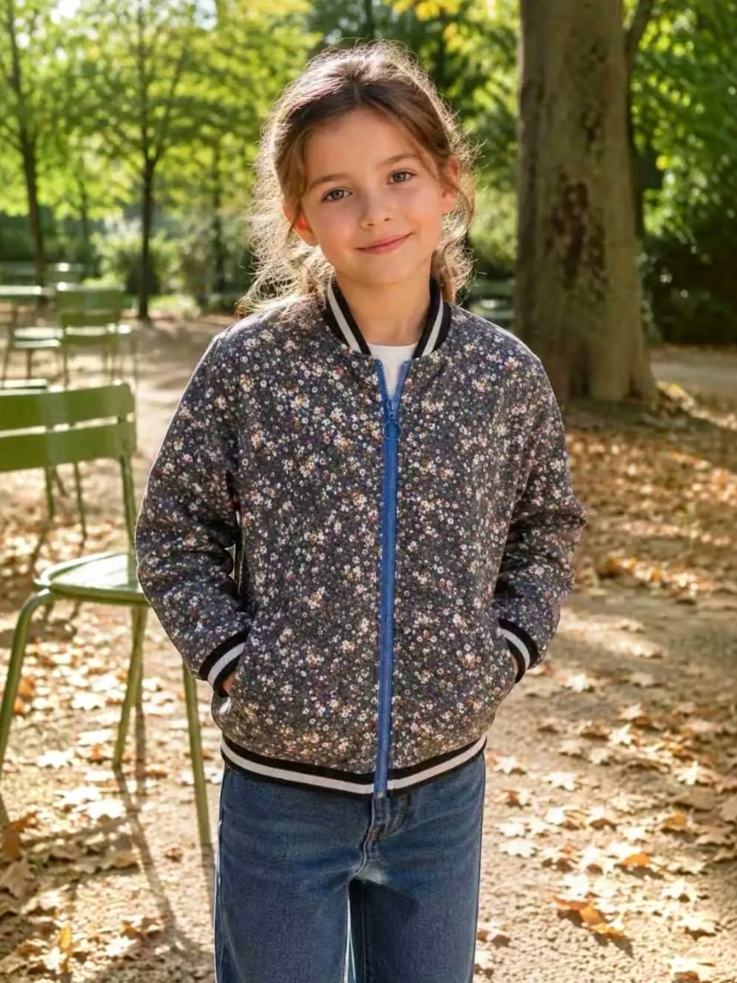 Young girl wearing a BROCK GRASSTAR floral print bomber jacket with a blue zipper in a park setting