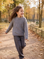 A young girl wearing a grey BROCK GRASSTAR knit sweater with cable texture, walking in an autumn park.