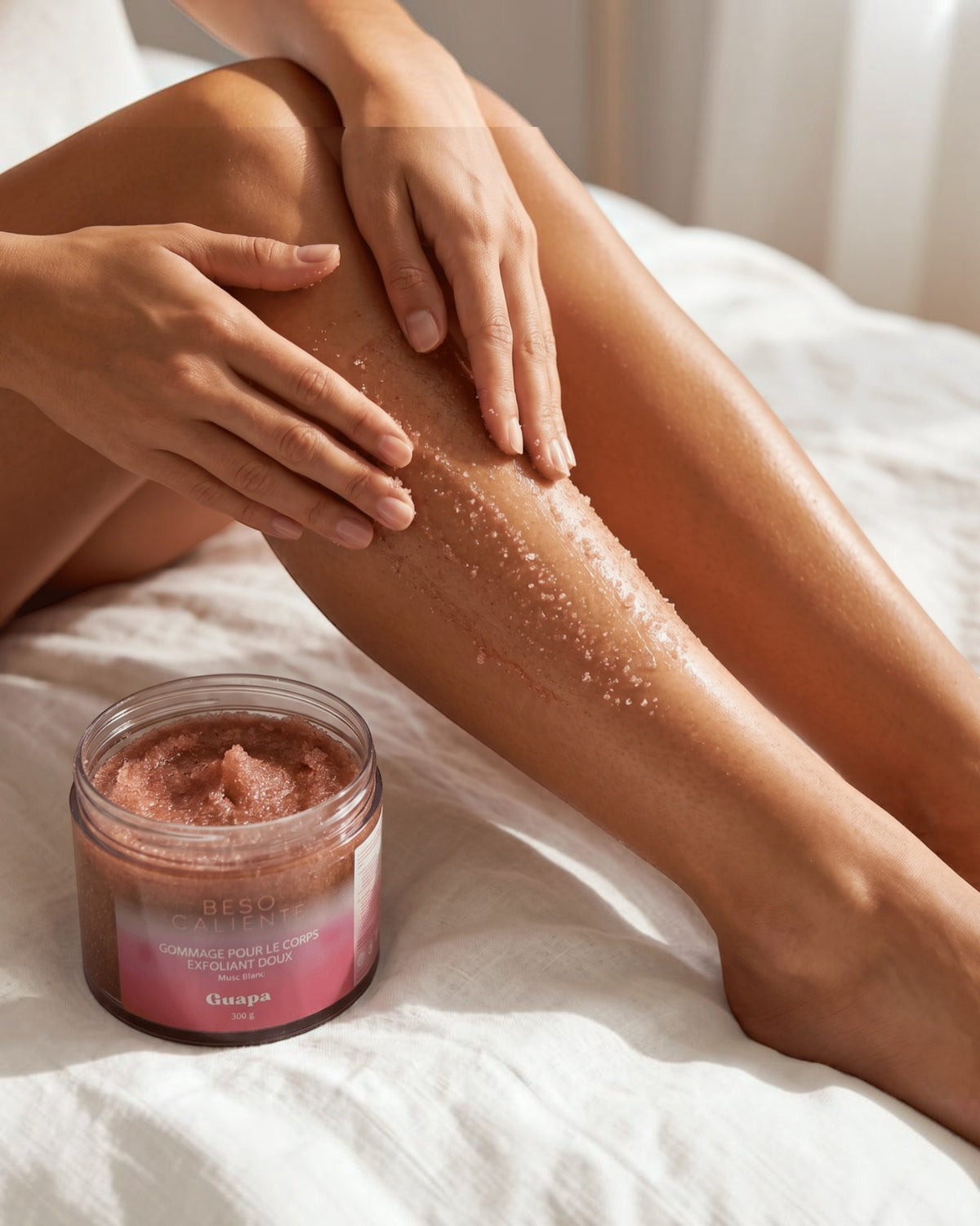 BROCK GUAPA Beso Caliente white musk body scrub being applied to a woman's leg for gentle exfoliation