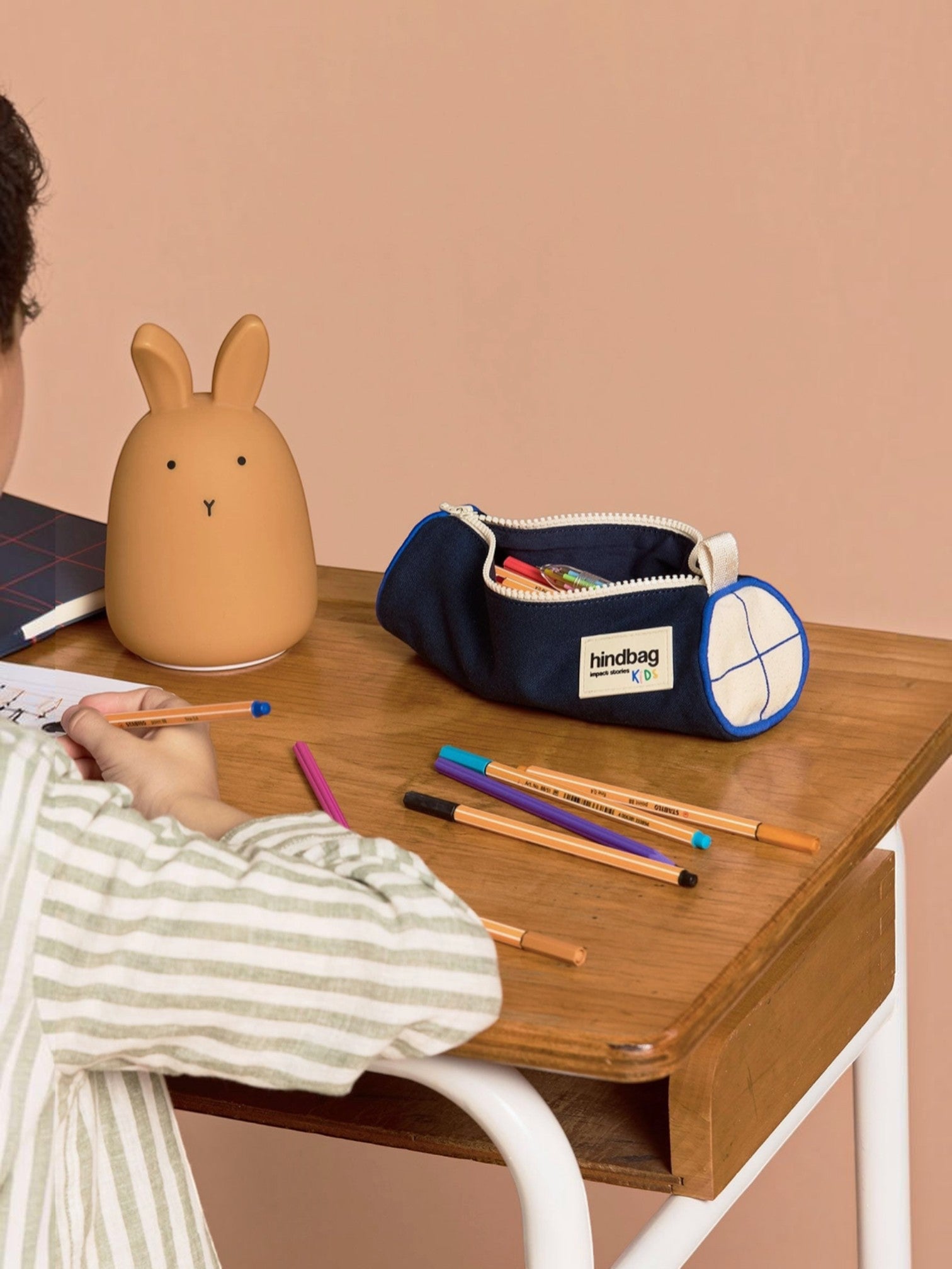 BROCK HINDBAG Mia round pencil case in dark blue with white accents on a wooden desk with a rabbit lamp