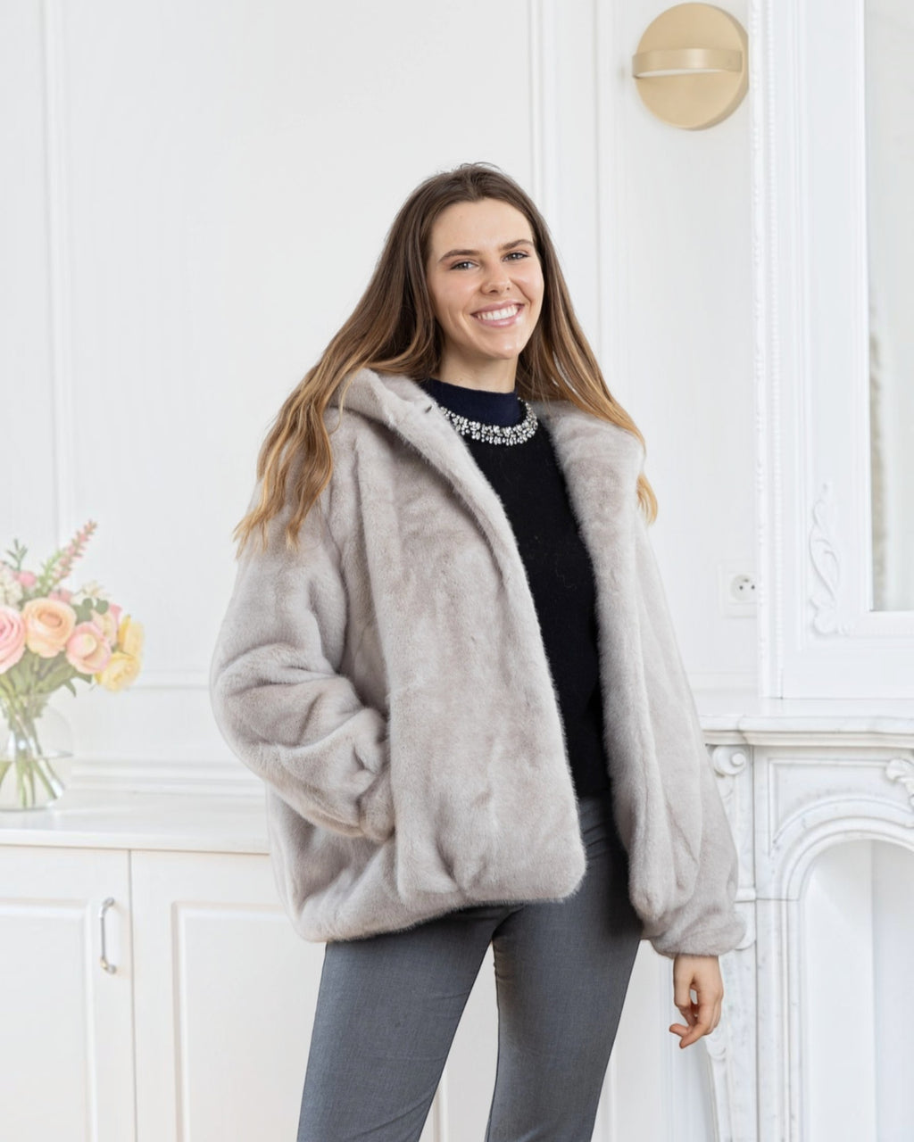 Woman wearing a BROCK LINETA beige faux fur hooded coat with a velvet-touch texture in a bright interior setting.