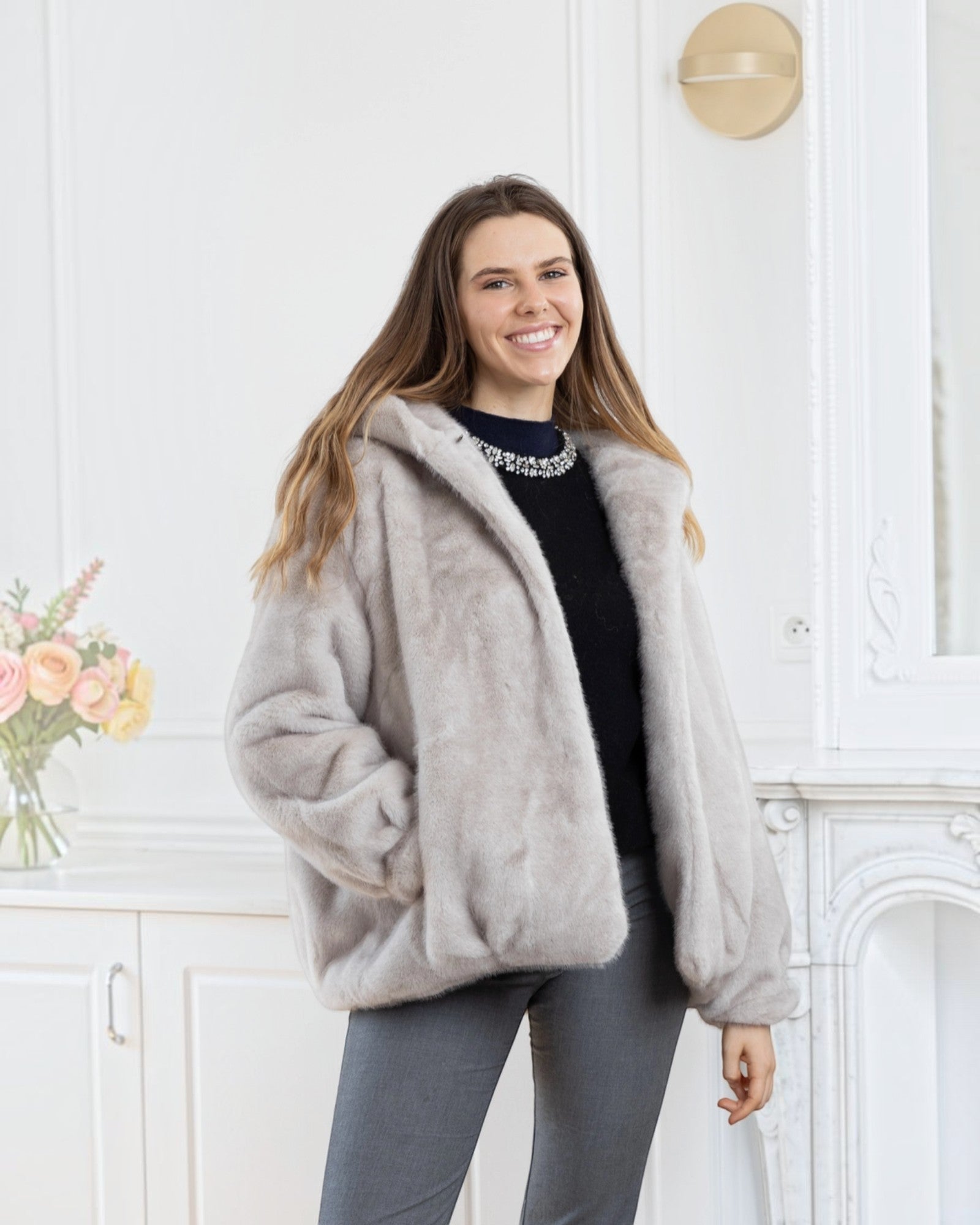 Woman wearing a BROCK LINETA beige faux fur hooded coat with a velvet-touch texture in a bright interior setting.
