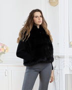 Model wearing a BROCK LINETA black faux fur sleeveless vest with a hood over a black sweater and grey trousers.
