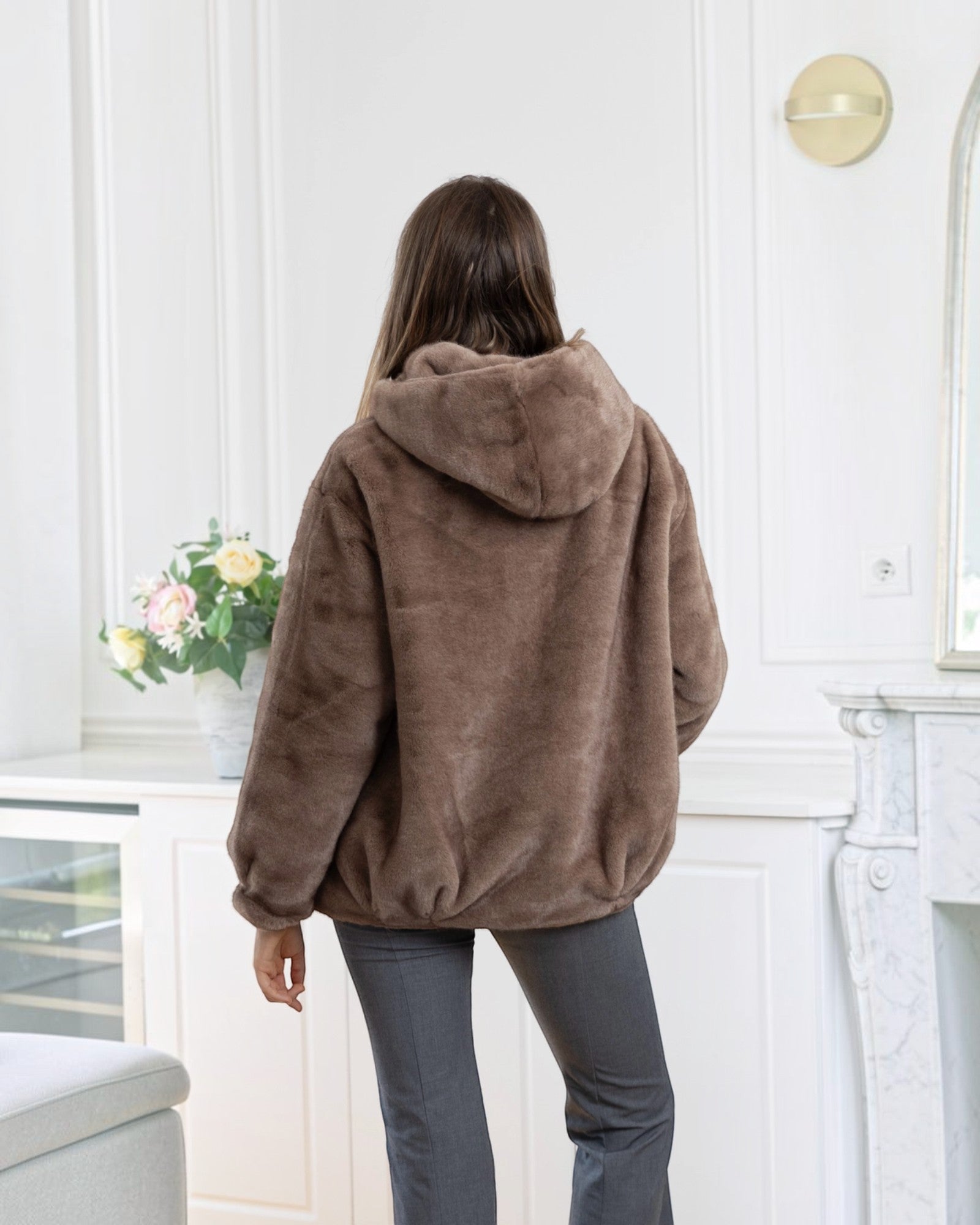 BROCK LINETA brown faux fur hooded coat with an oversized fit, worn by a woman in a bright interior.
