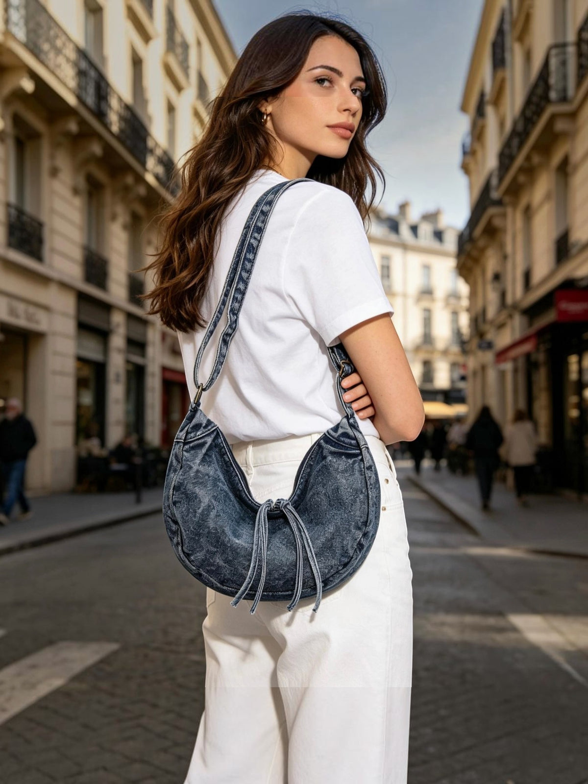 Woman wearing a BROCK LINETA denim-effect crescent crossbody bag with tassel detail on a city street