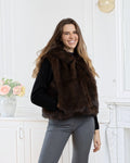 A smiling woman wearing a BROCK LINETA two-tone faux fur hooded vest over a black sweater and grey trousers.