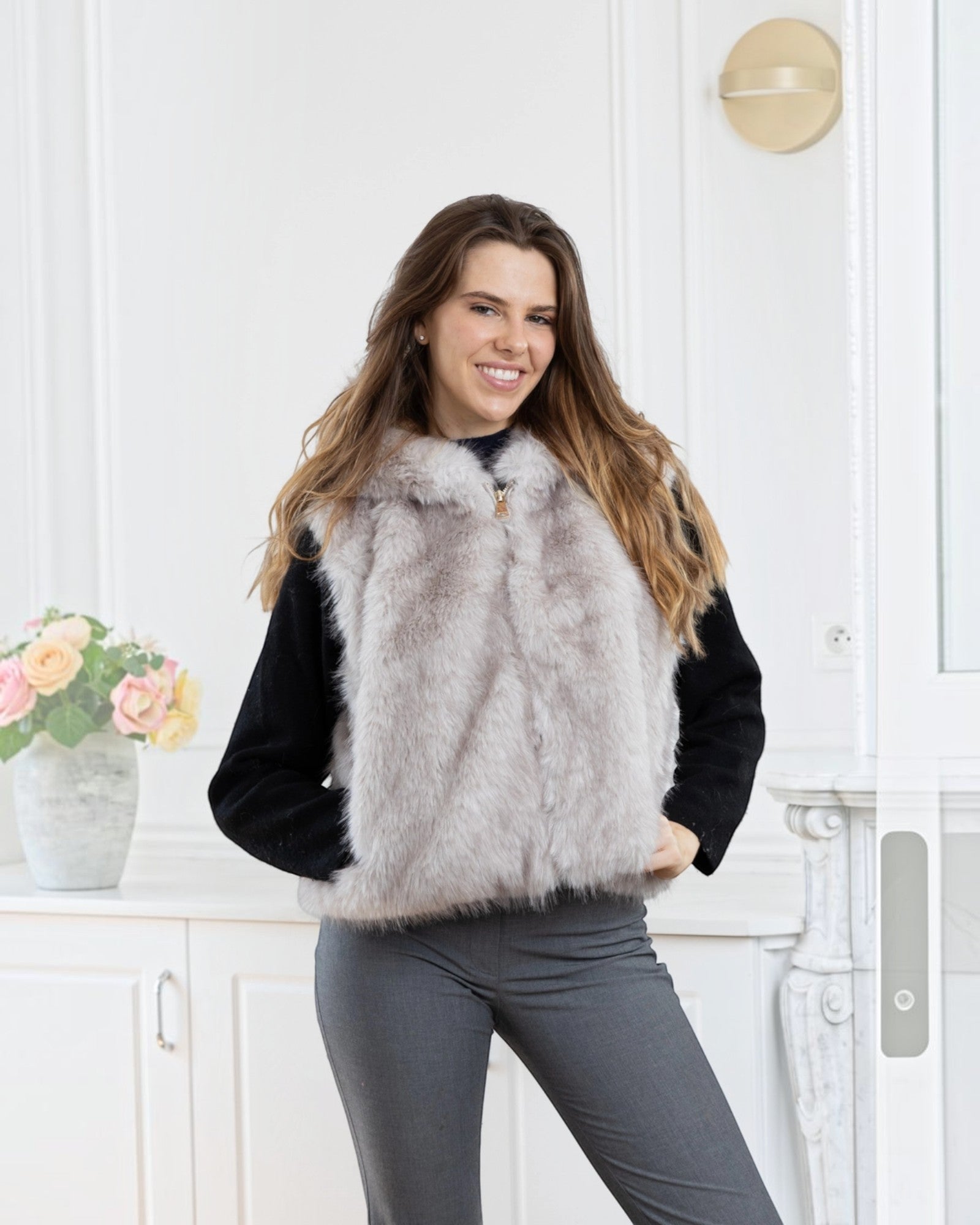 BROCK LINETA two-tone faux fur sleeveless vest with hood worn by a smiling woman in a bright interior