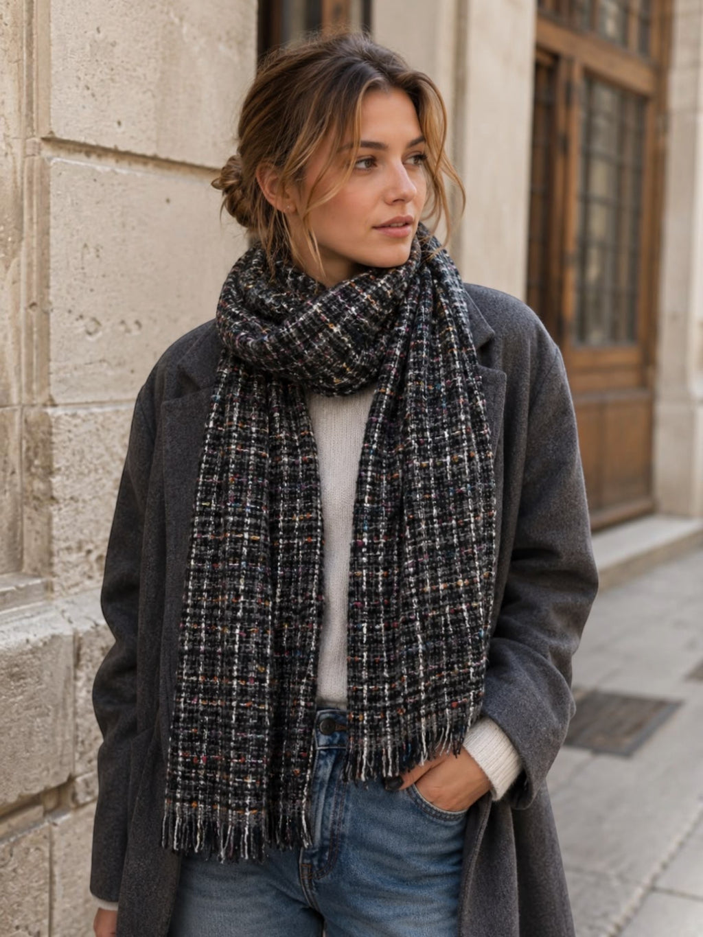 BROCK LINETA unisex scarf in a dark grey tweed pattern with multicoloured flecks, worn by a woman outdoors.