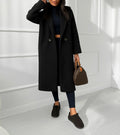 BROCK long black bouclé coat with a loose fit and button closure worn by a model in a bright studio setting