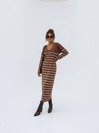 BROCK long brown striped maxi dress with V-neck and long sleeves worn by a model with brown boots and sunglasses