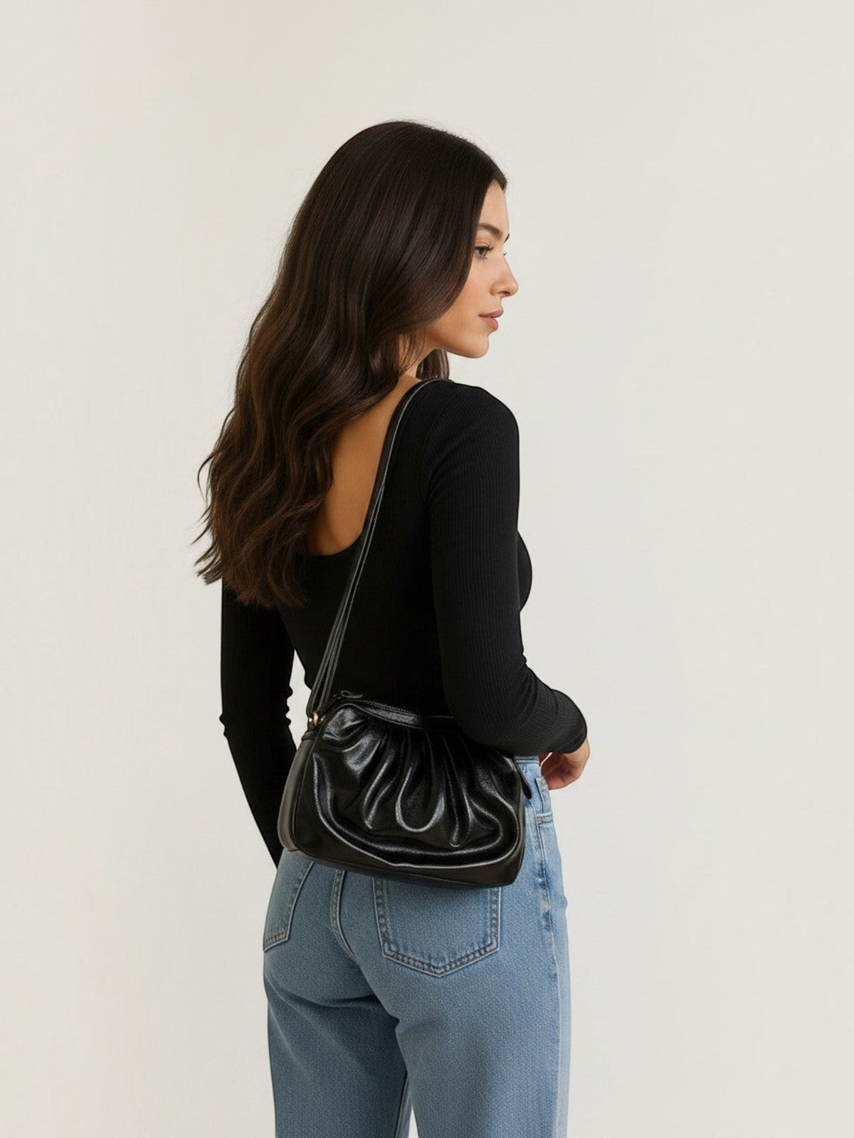Model wearing a BROCK LOUISA LEE black metallic leather croissant crossbody bag with a ruched design