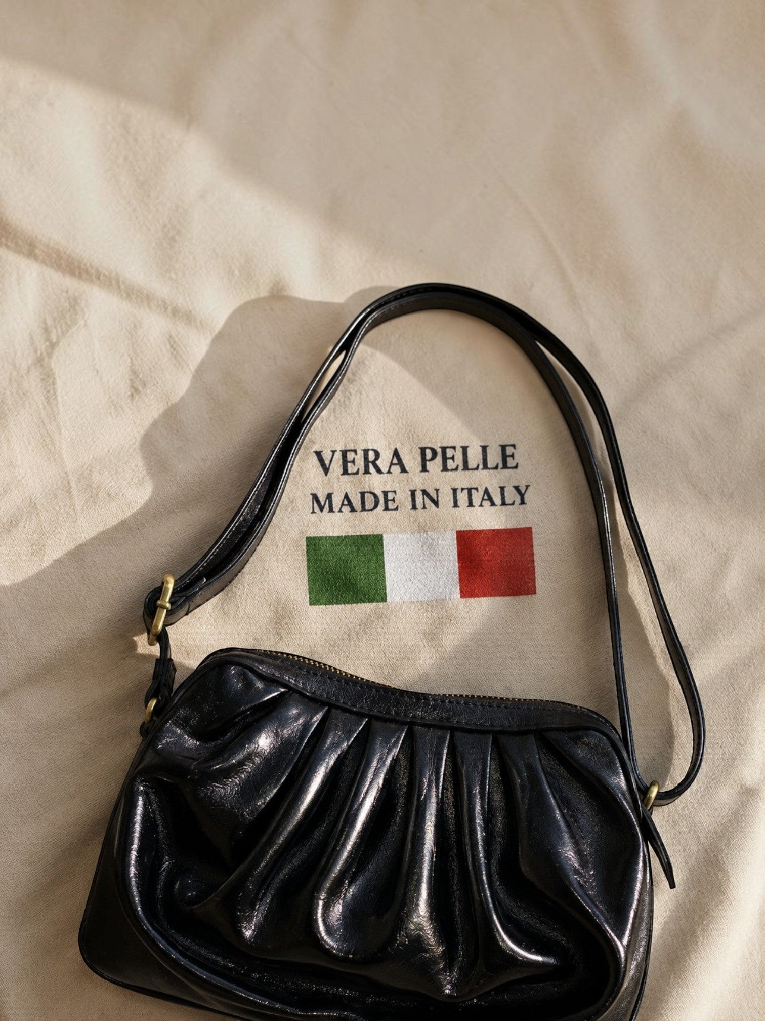 BROCK LOUISA LEE black metallic leather croissant shoulder bag with ruched design on a fabric background