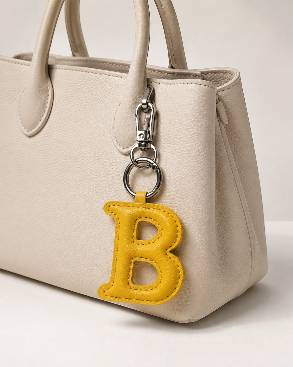 Charm bijou de sac BROCK LOUISA LEE en forme de lettre B jaune en tissu accroché à un sac à main beige en cuir