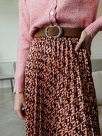 BROCK LOVIE & CO long pleated skirt with geometric print, satin finish, and elastic waist worn with a brown belt