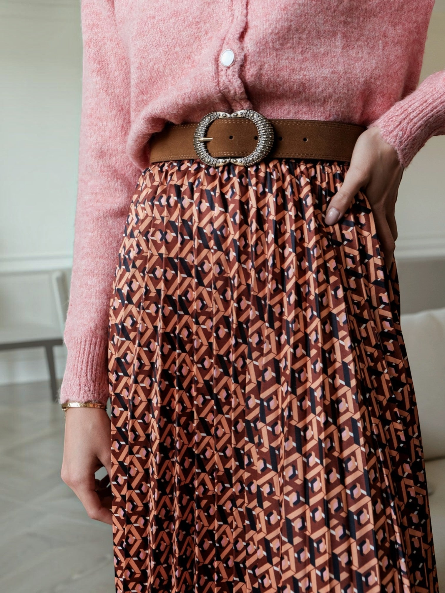 BROCK LOVIE & CO long pleated skirt with geometric print, satin finish, and elastic waist worn with a brown belt