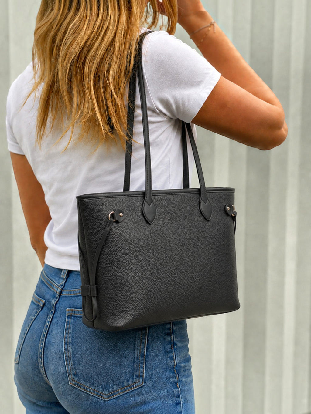 Woman wearing a black MIA LAROUGE university shoulder bag with adjustable straps and a textured leather finish.