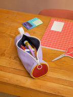 BROCK Mia tricolor pencil case in sage, purple, and red with a round design, filled with school supplies on a desk.