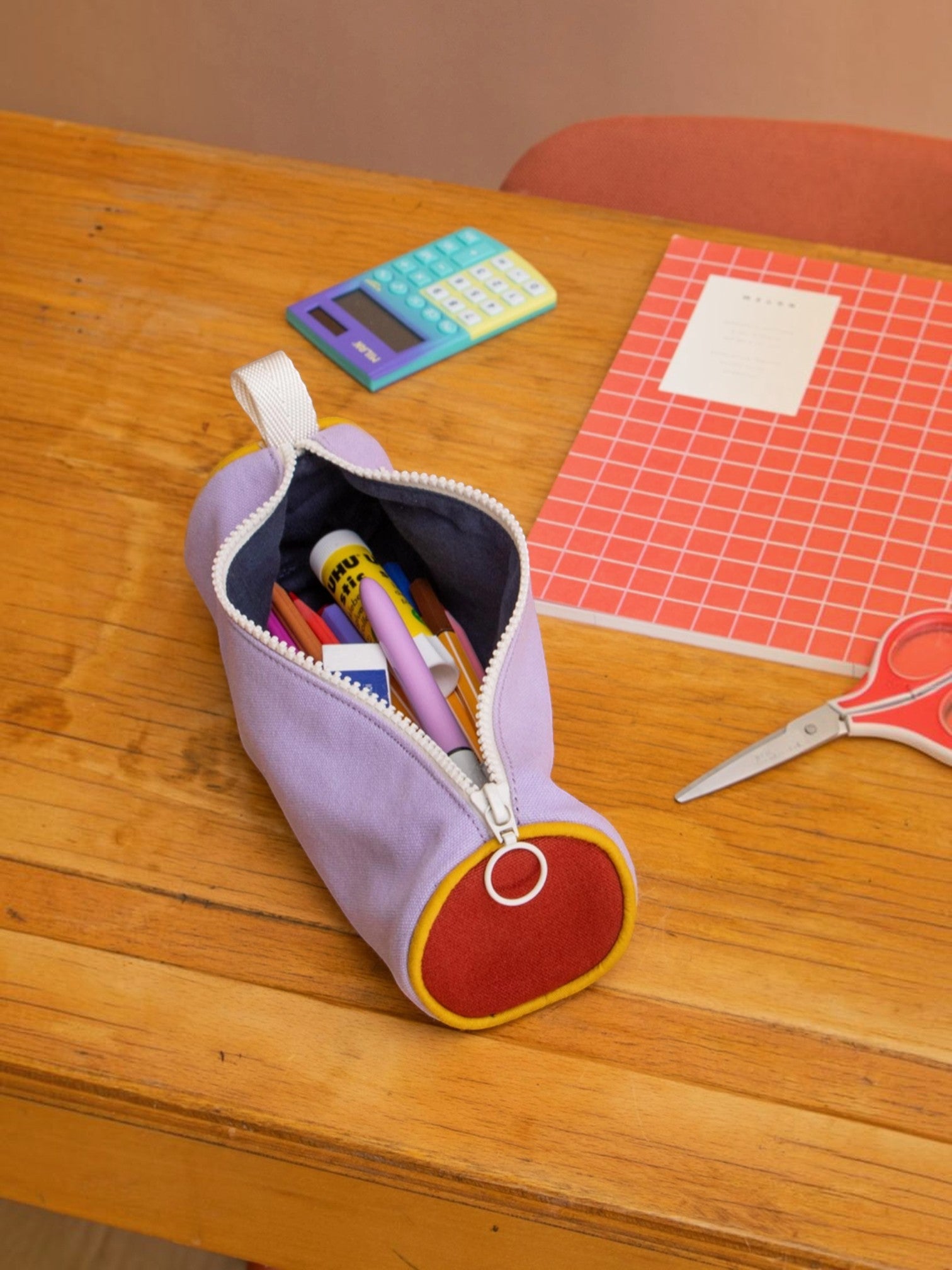 BROCK Mia tricolor pencil case in sage, purple, and red with a round design, filled with school supplies on a desk.