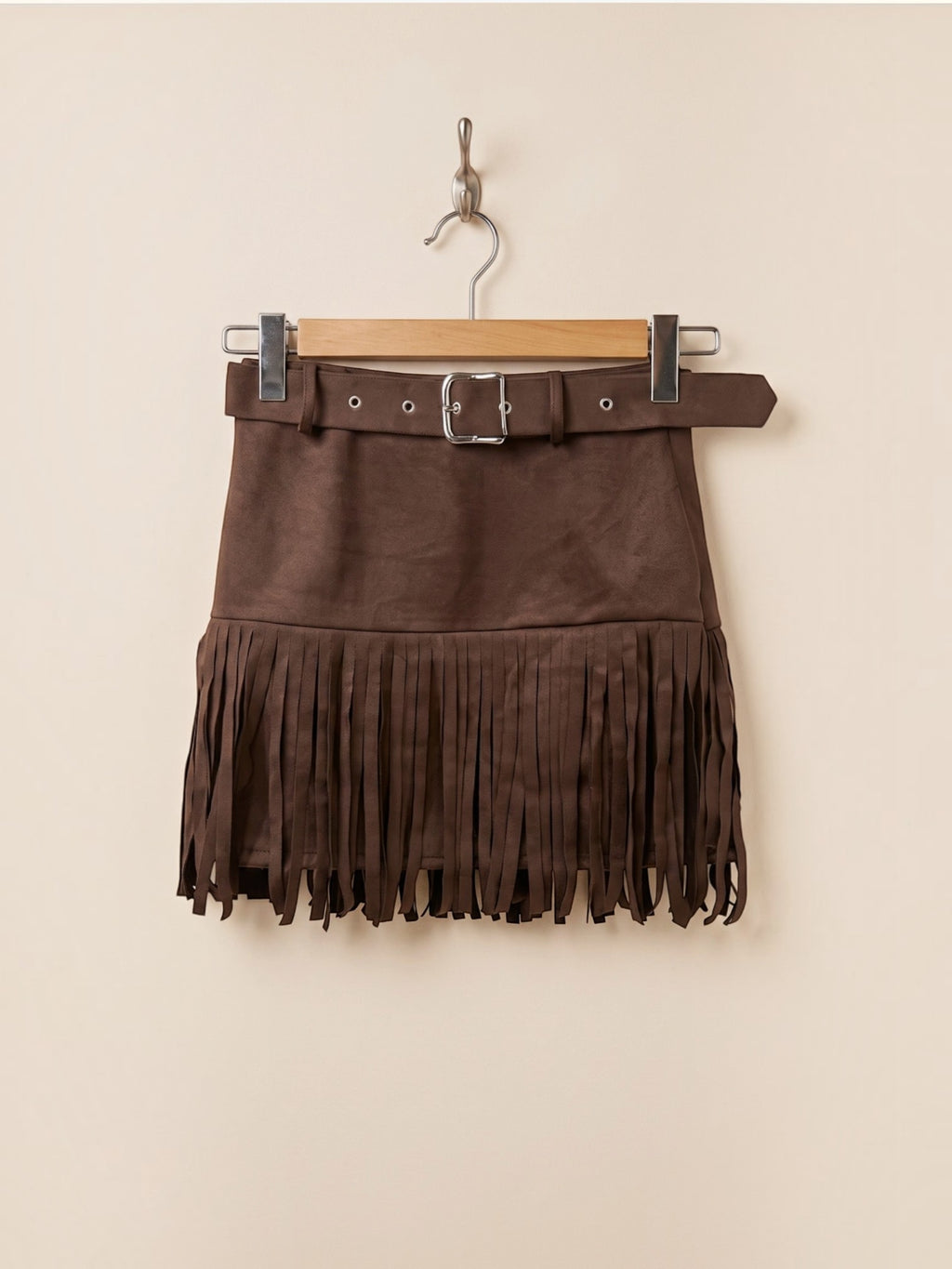 BROCK MOOYA brown faux suede mini skirt with fringe hem and matching belt with silver buckle hanging on a hanger