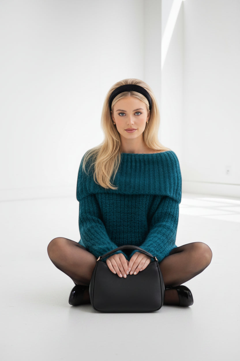 Model wearing a teal MOOYA Bardot sweater with a textured knit, black headband, and handbag in a bright studio space.