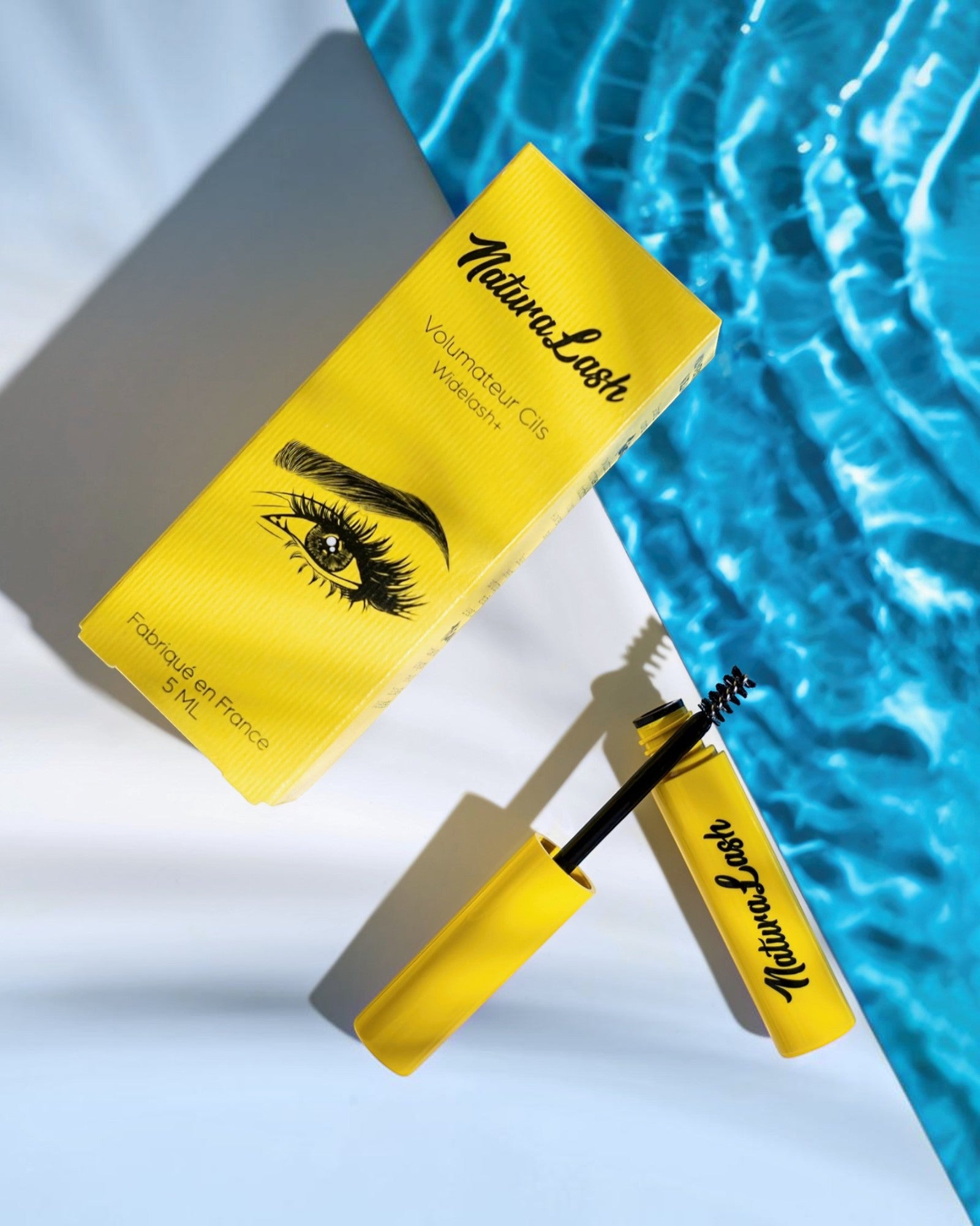 BROCK NATURALASH volumizing eyelash serum in a bright yellow tube and box, set against a blue water background.