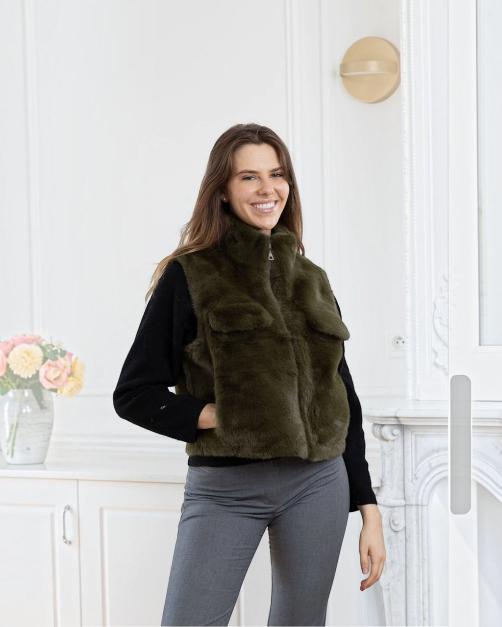 A woman wearing a BROCK olive green faux fur sleeveless vest with a zip closure and side pockets.