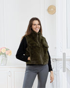 A woman wearing a BROCK olive green faux fur sleeveless vest with a zip closure and side pockets.