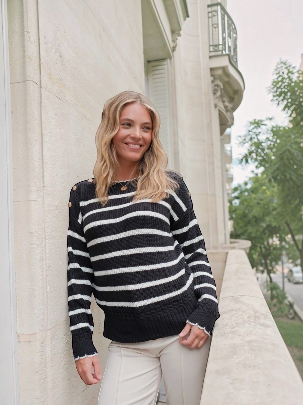 Femme souriante portant un pull marinière BROCK en coton noir et blanc avec boutons dorés sur les épaules