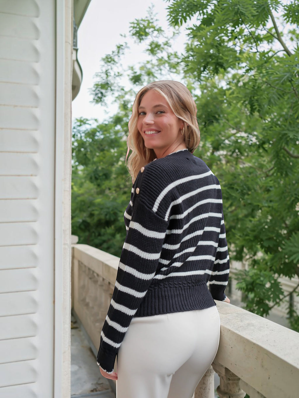 Femme souriante portant un pull marinière BROCK en maille de coton noir et blanc avec boutons dorés sur l'épaule