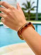 BROCK ROSA rigid bangle bracelet in translucent amber-colored resin with gold inclusions worn on a woman's wrist