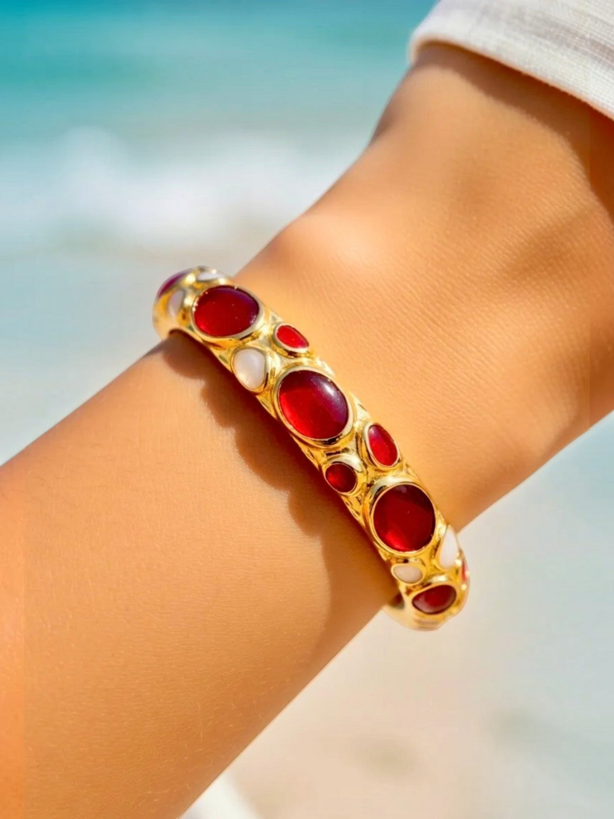 BROCK ROSA Thai-inspired brass bangle bracelet featuring polished red and white stones worn on a wrist at the beach