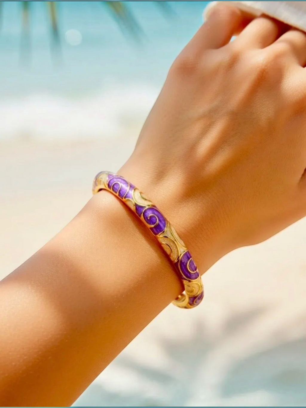 BROCK ROSA Thai-inspired brass bangle bracelet with purple and gold swirl patterns worn on a wrist at the beach