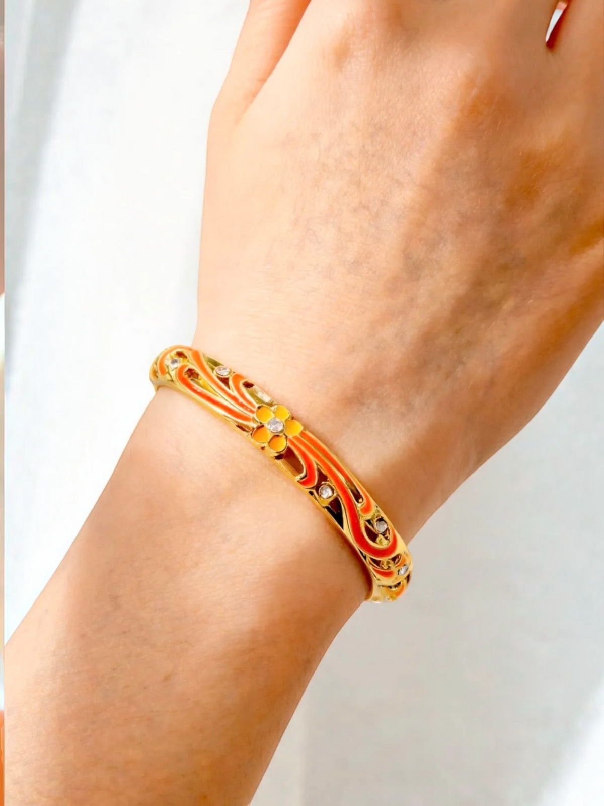 BROCK ROSA Thai-inspired brass bangle bracelet featuring orange and yellow floral enamel patterns on a wrist.