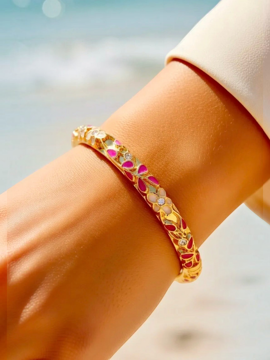 BROCK ROSA Thai-inspired brass bangle bracelet with pink and white floral enamel details worn on a wrist.