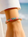 BROCK ROSA Thai-inspired brass bangle bracelet with pink and blue swirling patterns worn on a wrist at the beach.