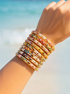 BROCK ROSA Thai-inspired brass bangles with colorful enamel and crystal accents stacked on a wrist at the beach.