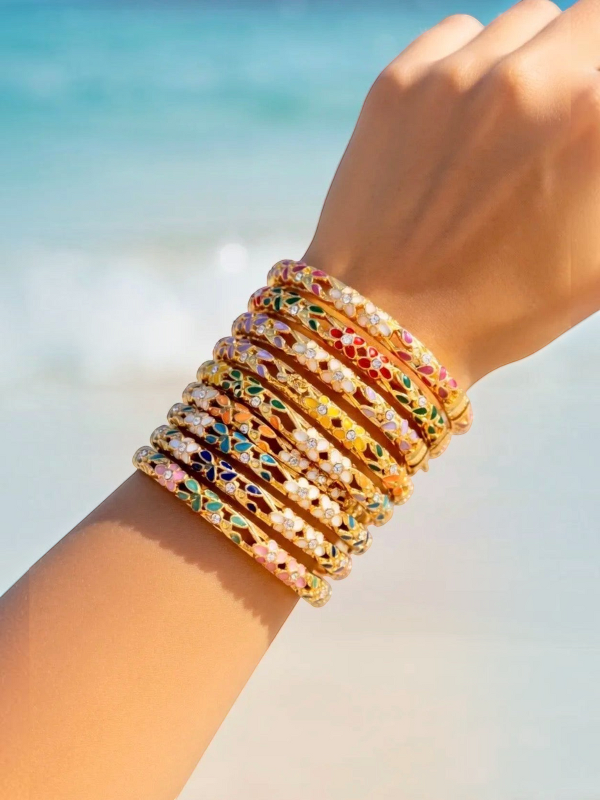 BROCK ROSA Thai-inspired brass bangles with colorful enamel and crystal accents stacked on a wrist at the beach.