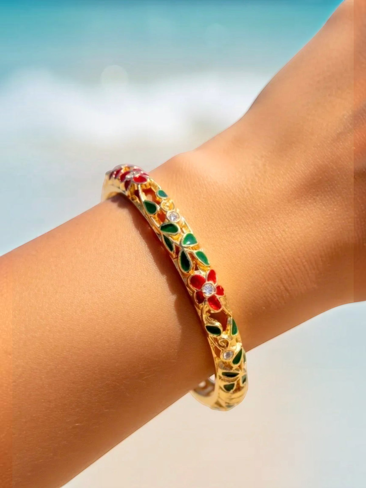 BROCK ROSA Thai-inspired brass bangle bracelet with red and green floral enamel details worn on a wrist.