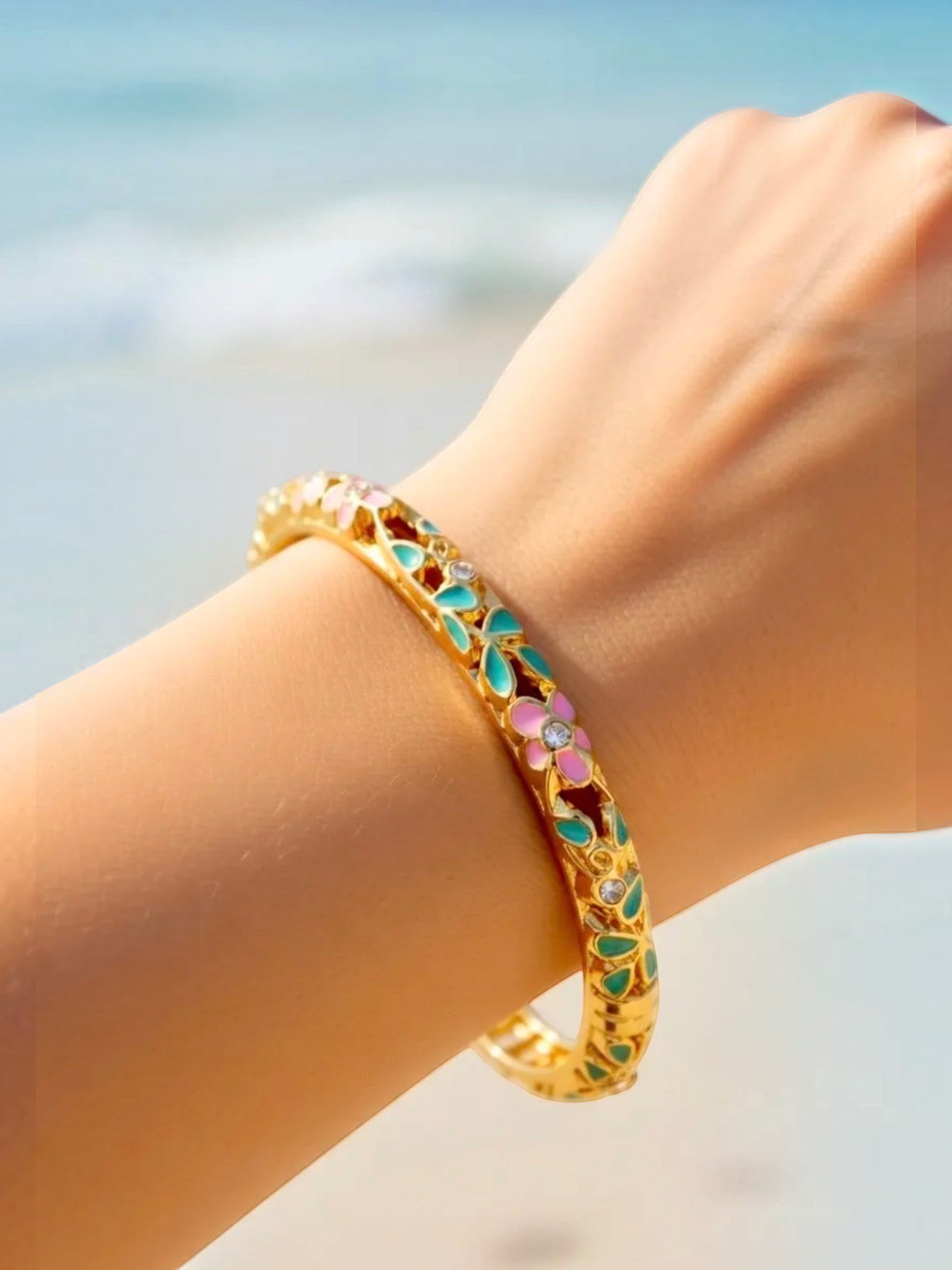 BROCK ROSA Thai-inspired gold brass bangle bracelet with colorful floral enamel and crystal accents on a wrist.