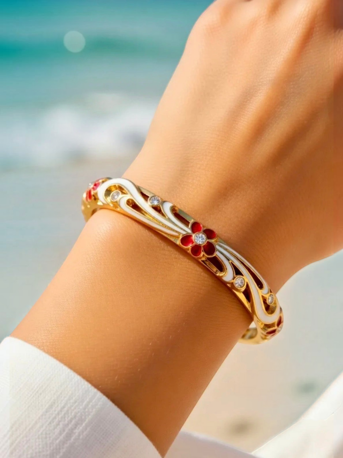 BROCK ROSA Thai-inspired gold brass bangle bracelet featuring white enamel and red floral details on a wrist.