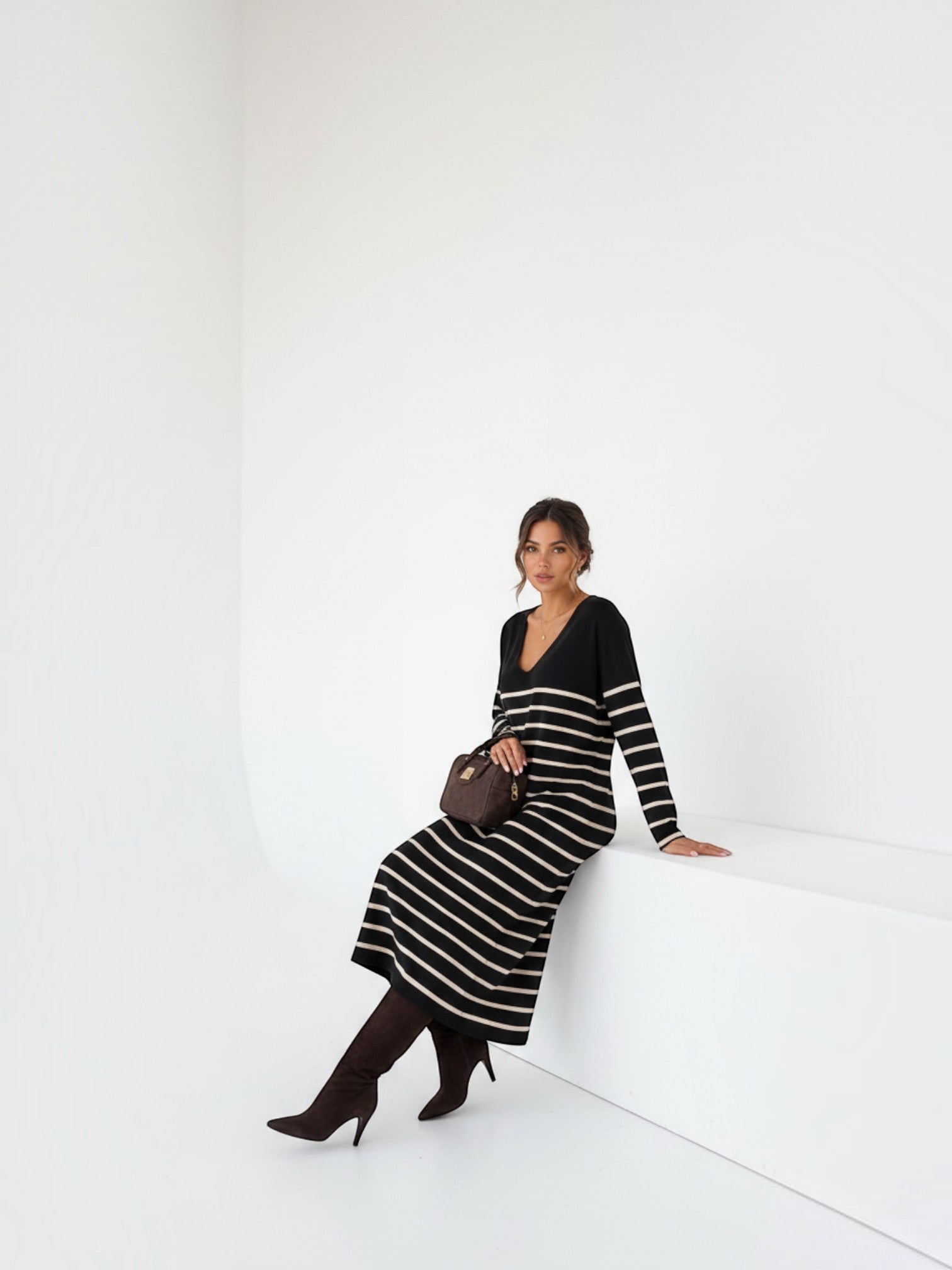 Model wearing a BROCK long-sleeved striped maxi dress with a V-neck, styled with dark boots in a minimalist studio.