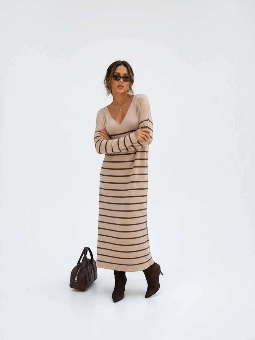Model wearing a BROCK long-sleeved maxi dress with V-neck and brown stripes, styled with dark boots and sunglasses.