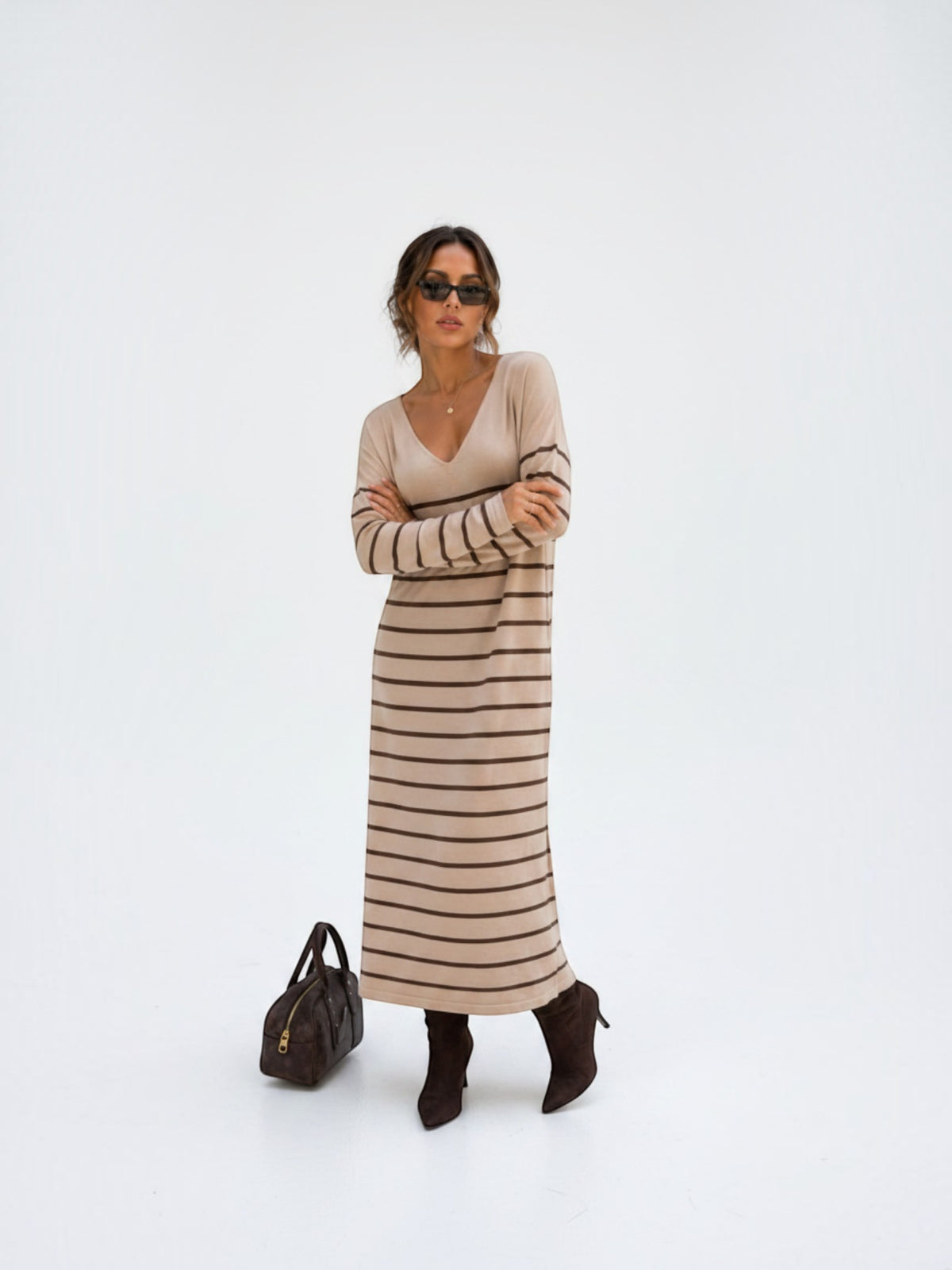 Model wearing a BROCK long-sleeved maxi dress with V-neck and brown stripes, styled with dark boots and sunglasses.