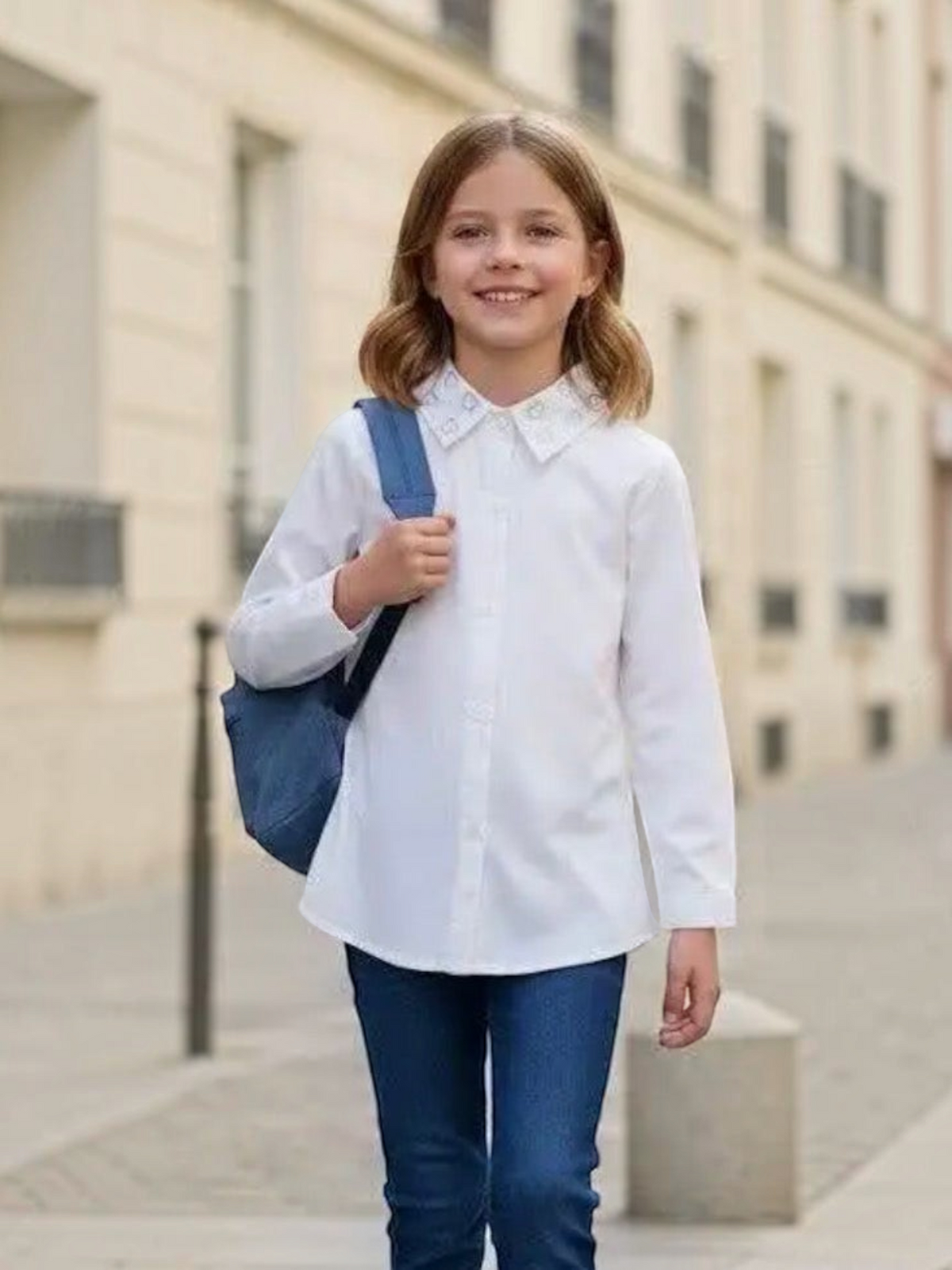 A young girl wearing a white BROCK cotton shirt with heart-shaped rhinestones on the collar, walking outdoors.