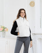 Model wearing a white BROCK faux fur sleeveless vest with a zip closure and side pockets in a bright room.