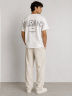 Man wearing a white BROCK cotton t-shirt with a large black typographic graphic print on the back, view from behind.