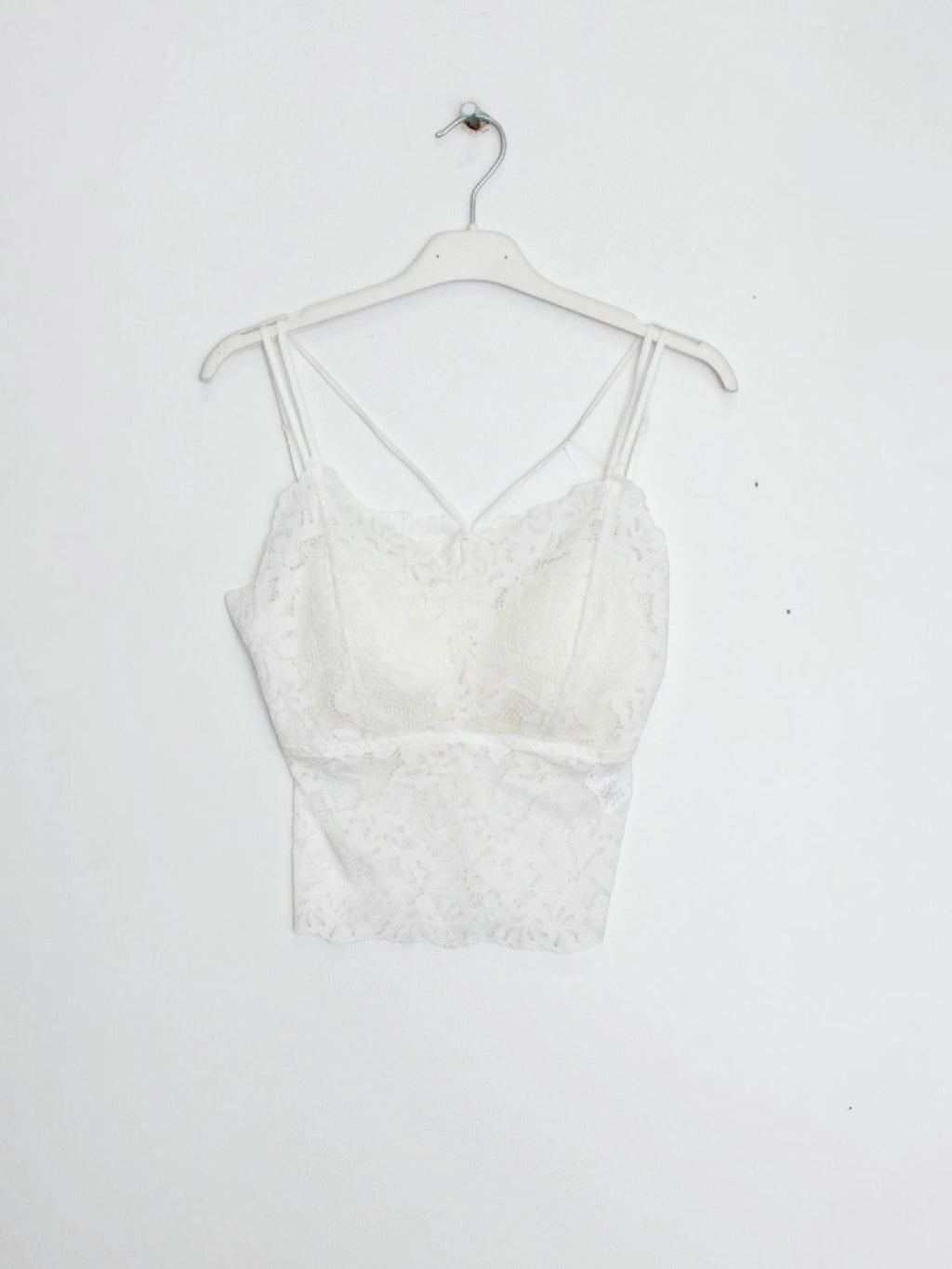 BROCK white lace crop top tank with built-in cups and delicate spaghetti straps hanging on a white hanger
