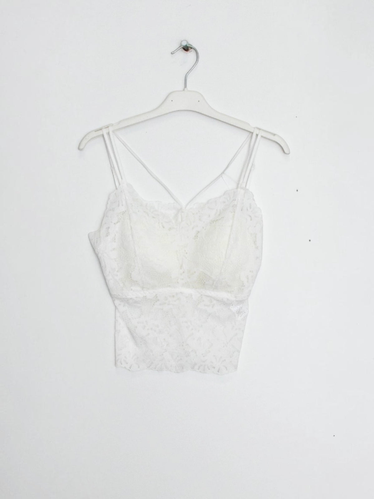 BROCK white lace crop top tank with built-in cups and delicate spaghetti straps hanging on a white hanger